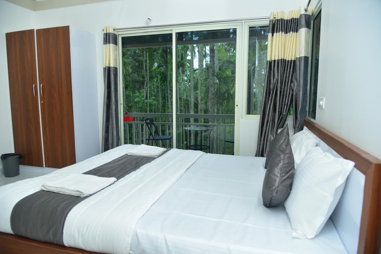 A bed beside a glass door that opens to the balcony and palm trees